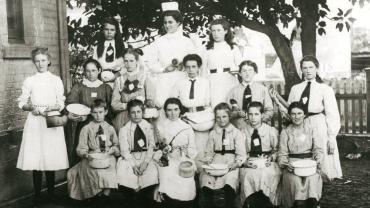 Cooking classes in public schools were established in 1897. This group shows girls holding basins, pots, spoons and what may be a rolling pin. The teacher is wearing apron and cap. Burwood Public School Cookery Class, 1908. Digital ID 15051_a047_002139